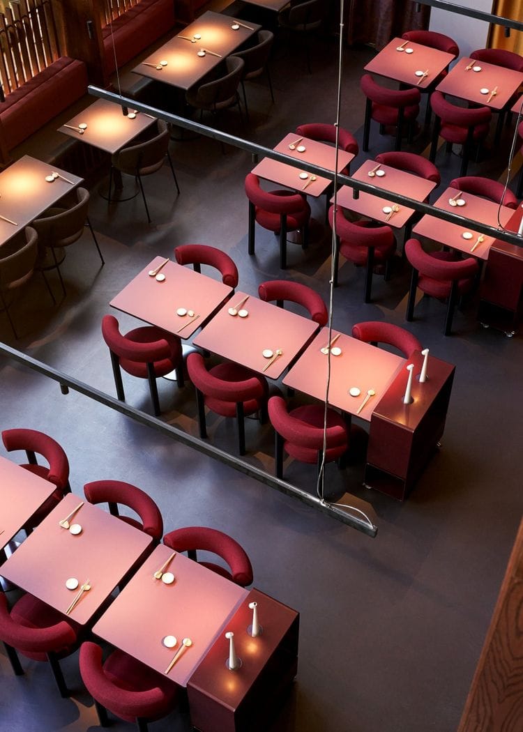Top-down view of a modern restaurant with red upholstered chairs and pink square tables set with chopsticks and spoons.